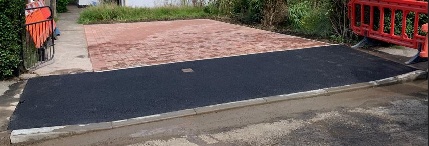 Fresh tarmac dropped kerb crossing to a block paved driveway by Drop Kerbs UK